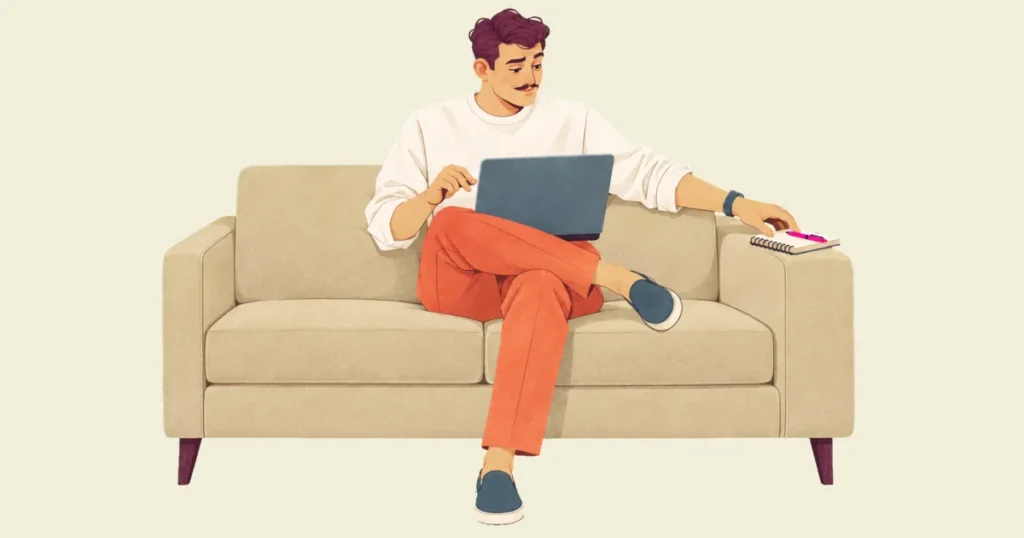 Ivo on a sofa with his laptop on his knees, one hand hovering over it, reaches for a notebook and pink pen on the armrest instead.